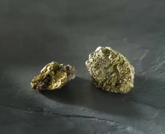 A lump of real gold next to a lump of fool's gold on slate.