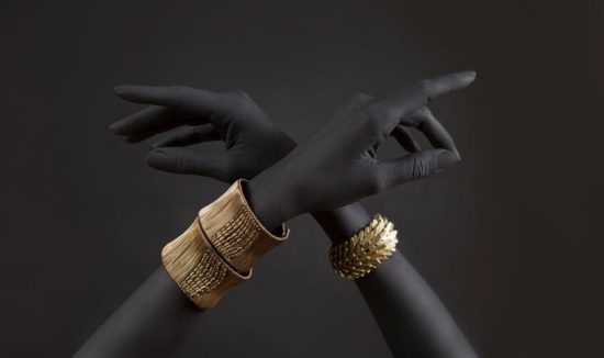 A pair of hands with three gold bracelets on them.