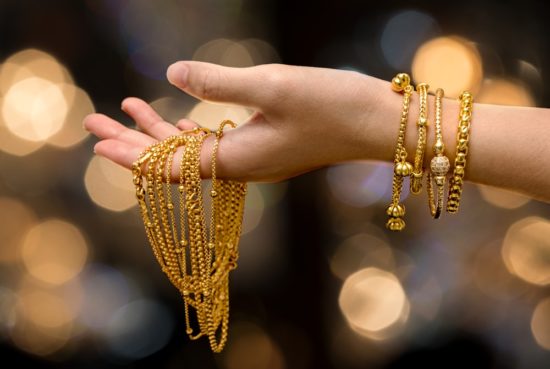 A hand with a gold necklace with gold bracelets on the wrist.