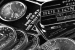 Silver bullion bars and one troy ounce fine silver coins scattered on a dark reflective surface