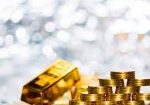 Stacked gold coins arranged in pyramid formation beside a shiny gold bullion bar on reflective surface